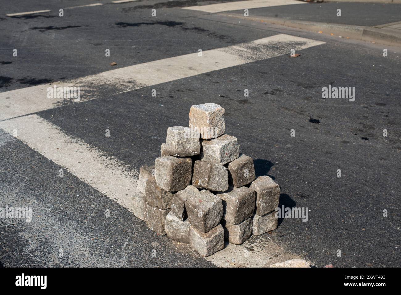 Ein Haufen Ziegelsteine, die nach einem Aufstand ordentlich auf einer städtischen Straße gestapelt wurden. Dieses Bild zeigt eine Szene des Chaos und des Wiederaufbaus und symbolisiert Widerstandsfähigkeit und Erholung. Stockfoto