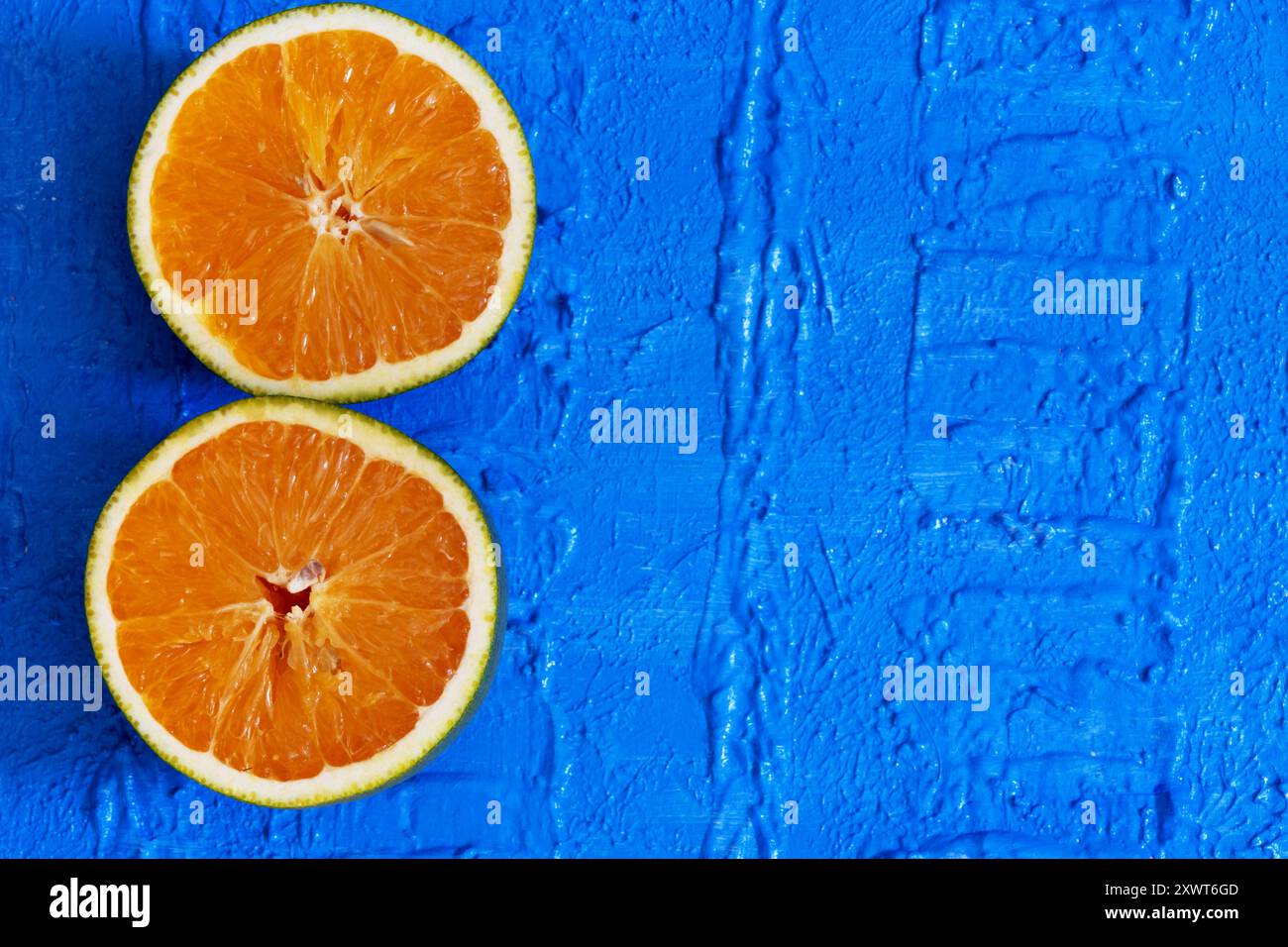 Zwei Teile einer Orange auf einem strukturierten blauen Tisch. Stockfoto