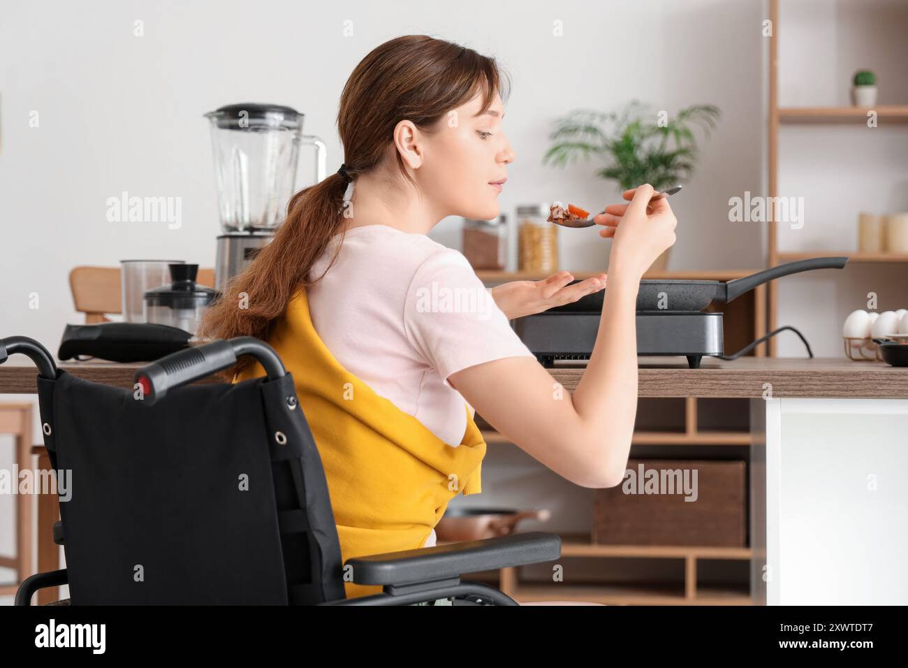 Junge Frau im Rollstuhlverkostung zu Hause Stockfoto