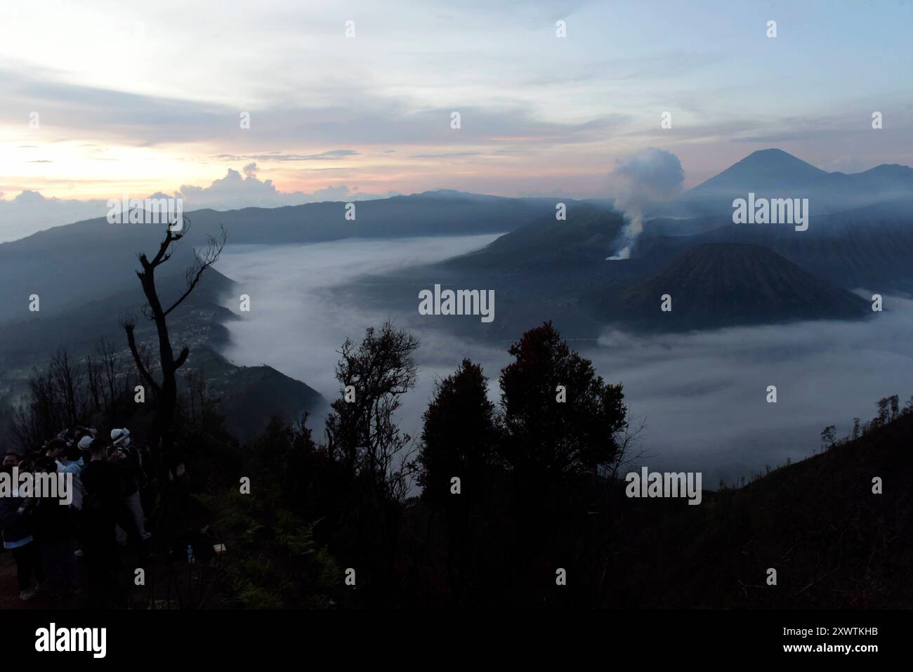 Menschen kommen, um sich den Sonnenaufgang über der Tengger-Caldera anzusehen. Links ist der Bromo rauchender Krater / Höhe: 2,329 Meter und rechts vorne der Batok zu sehen, im Hintergrund der Vulkan Semeru mit 3676 m Höhe der höchste Berg der indonesischen Insel Java. Der Nationalpark Bromo-Tengger-Semeru besteht seit 1982. Der mittlere Teil des Namens verweist auf das hier lebende Volk der Tengger. Zum Nationalpark gehören der 3676 m hohe Stratovulkan Semeru, der höchste Berg der Insel, sowie vier in der Tengger-Caldera liegende Vulkane, deren Bekanntester der Bromo ist. Die Caldera wird vom Stockfoto