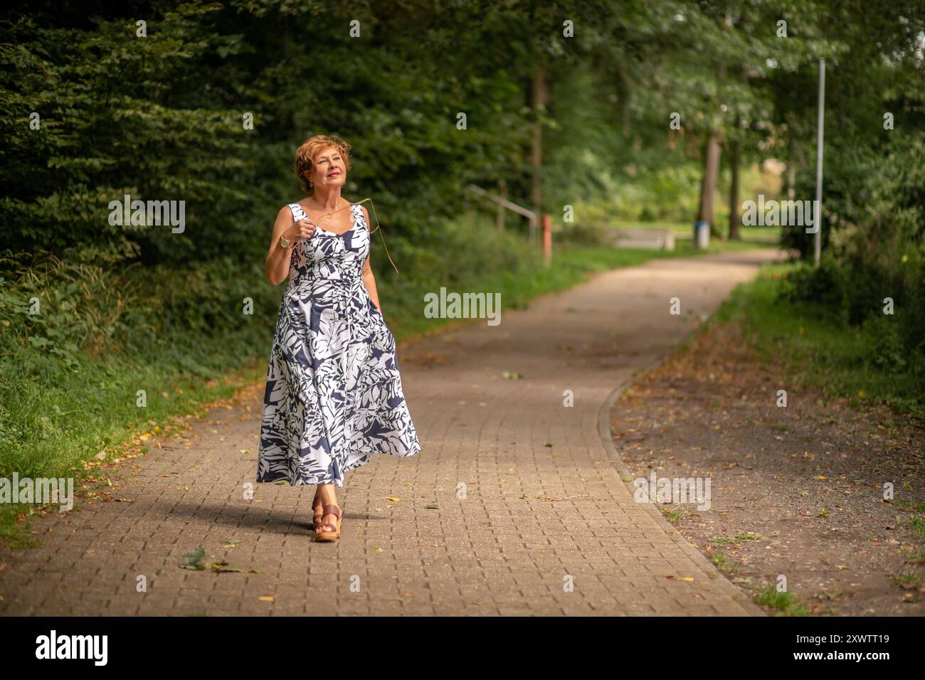 Eine Frau genießt einen gemütlichen Spaziergang entlang eines ruhigen Weges umgeben von lebhaftem Grün. Stockfoto