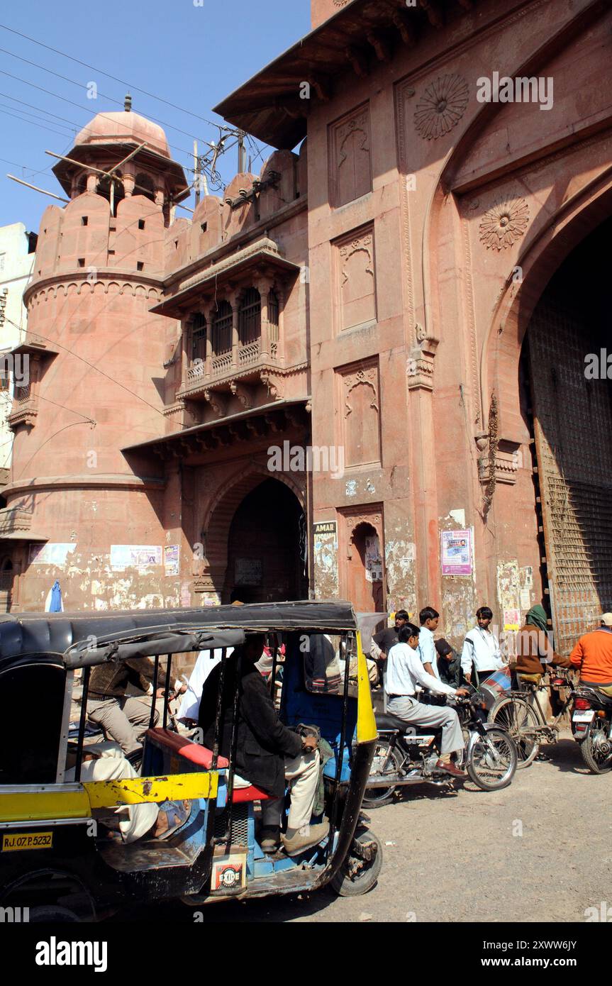 Menschen, Fahrräder und eine bunte Auto-Rikscha fahren zum alten Tor der Altstadt von Bikaner in Rajasthan, Indien Stockfoto