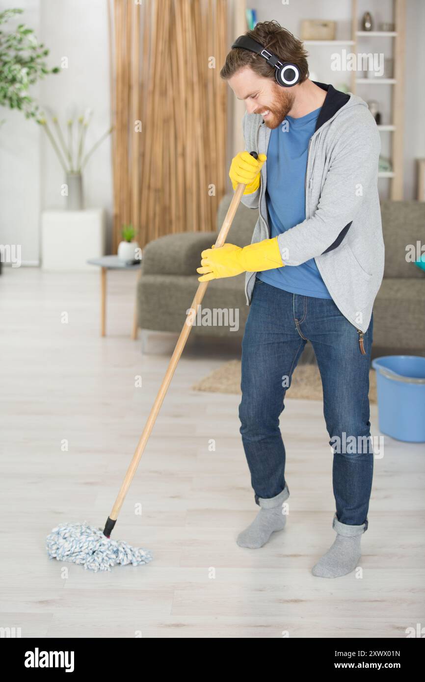 Glücklicher Mann mit Wischmopp und Eimer, der zu Hause den Boden reinigt Stockfoto