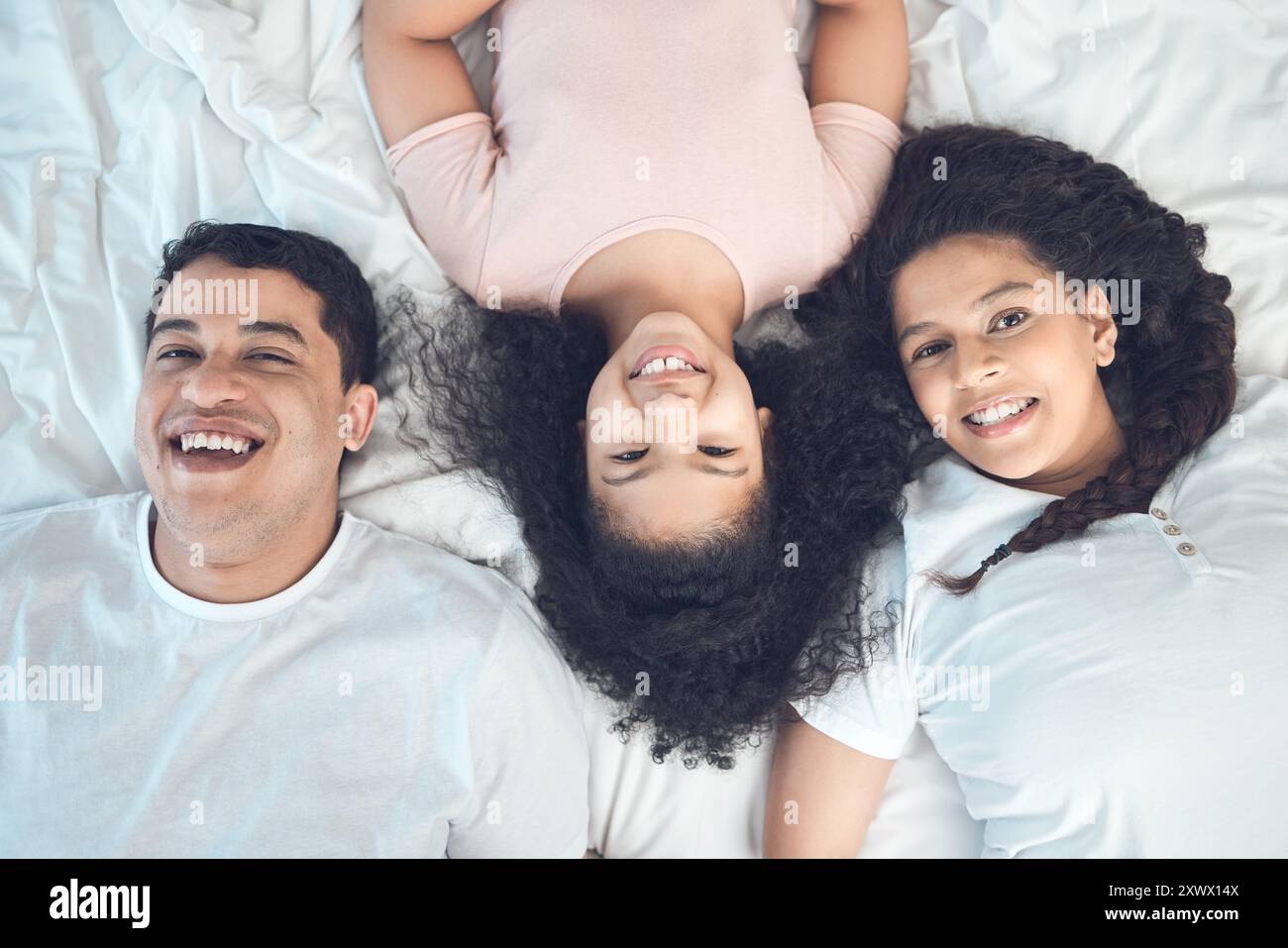 Mama, Vater und Kind im Porträt auf dem Bett mit Lächeln, Liebe und Entspannung am Morgen zusammen von oben. Mutter, Vater und Mädchenkind, die sich im Schlafzimmer verbünden Stockfoto