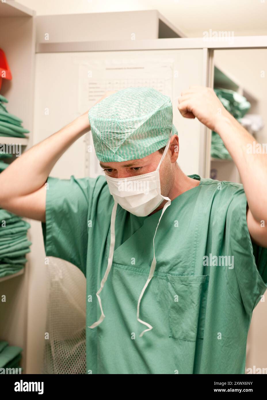 Ein Chirurg passt vor der Operation seine Kappe und Maske an und betont damit die Hygiene und Vorbereitung im Krankenhaus. Das Bild zeigt die sorgfältige Detailtreue und Professionalität, die in einer medizinischen Umgebung erforderlich sind. Stockfoto