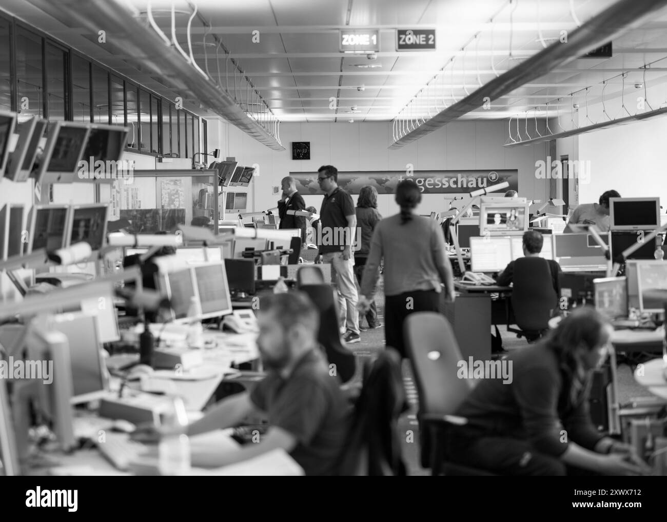 Schwarzweißbild, das die dynamische Umgebung im Tagesschau-Newsroom in Hamburg zeigt. Journalisten und Redakteure arbeiten in einem Meer von Monitoren zusammen, um das Wesen der Medienproduktion und Teamarbeit zu erfassen. Stockfoto