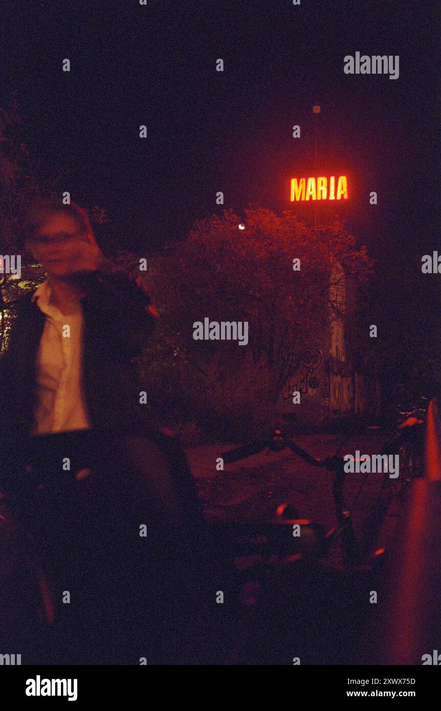 Eine verschwommene Figur bewegt sich an einem neonfarbenen „MARIA“-Schild vor dem dunklen Hintergrund des Club Maria am Ostbahnhof in Berlin-Friedrichshain vorbei. Das Bild zeigt Nachtleben, Geheimnisse und urbane Entdeckungen. Stockfoto Eine verschwommene Figur bewegt sich an einem neonfarbenen „MARIA“-Schild vor dem dunklen Hintergrund des Club Maria am Ostbahnhof in Berlin-Friedrichshain vorbei. Das Bild zeigt Nachtleben, Geheimnisse und urbane Entdeckungen. Stockfoto