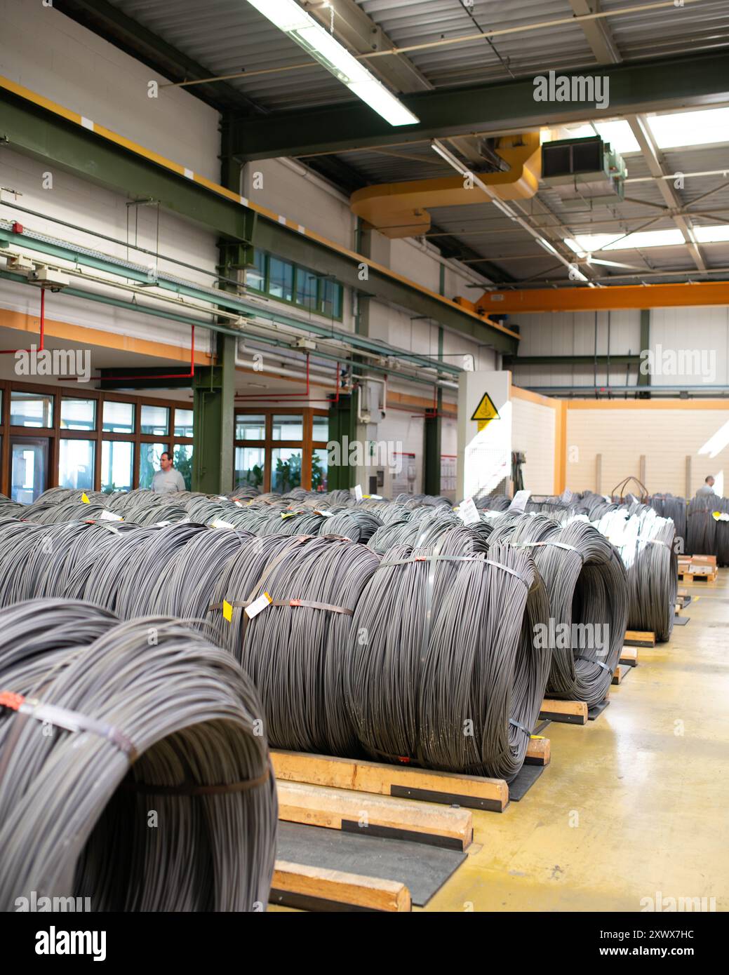 Geräumiges Industrielager mit großen, ordentlich gestapelten Metalldrahtspulen. Die Szene ist ideal für Fertigung und Vertrieb und spiegelt Organisation und Effizienz wider und unterstreicht die Rolle von Rohstoffen in der industriellen Produktion. Stockfoto