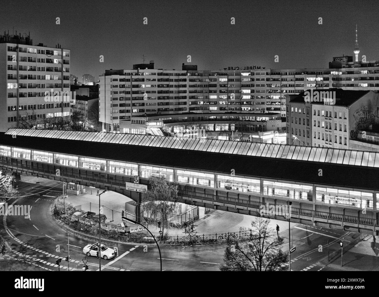 Das Schwarzweißbild des Kottbusser Tors im Berliner Kreuzberg zeigt urbane Architektur und das geschäftige Stadtleben bei Nacht. Das Foto weckt Gefühle von Verbundenheit und Einsamkeit, eine Metapher für die Dualität des modernen Lebens. Stockfoto