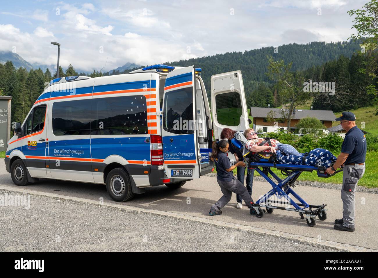 Oberstdorf, Deutschland. August 2024. Rima Schucht (l-r), Anita Sräga und Norbert Rzadki vom Arbeiter-Samariter-Bund (ASB) laden Kerstin Lindemann, die auf einer Liege liegt, in einen Krankenwagen auf der Alpe Dornach. Unter dem Motto „trauen Sie sich, letzte Wünsche zu machen“ bringt das ASB Patienten, die sich einer Behandlung unterziehen, an besondere Orte, um ihre letzten Wünsche zu erfüllen und besondere Erlebnisse zu ermöglichen. Quelle: Stefan Puchner/dpa/Alamy Live News Stockfoto