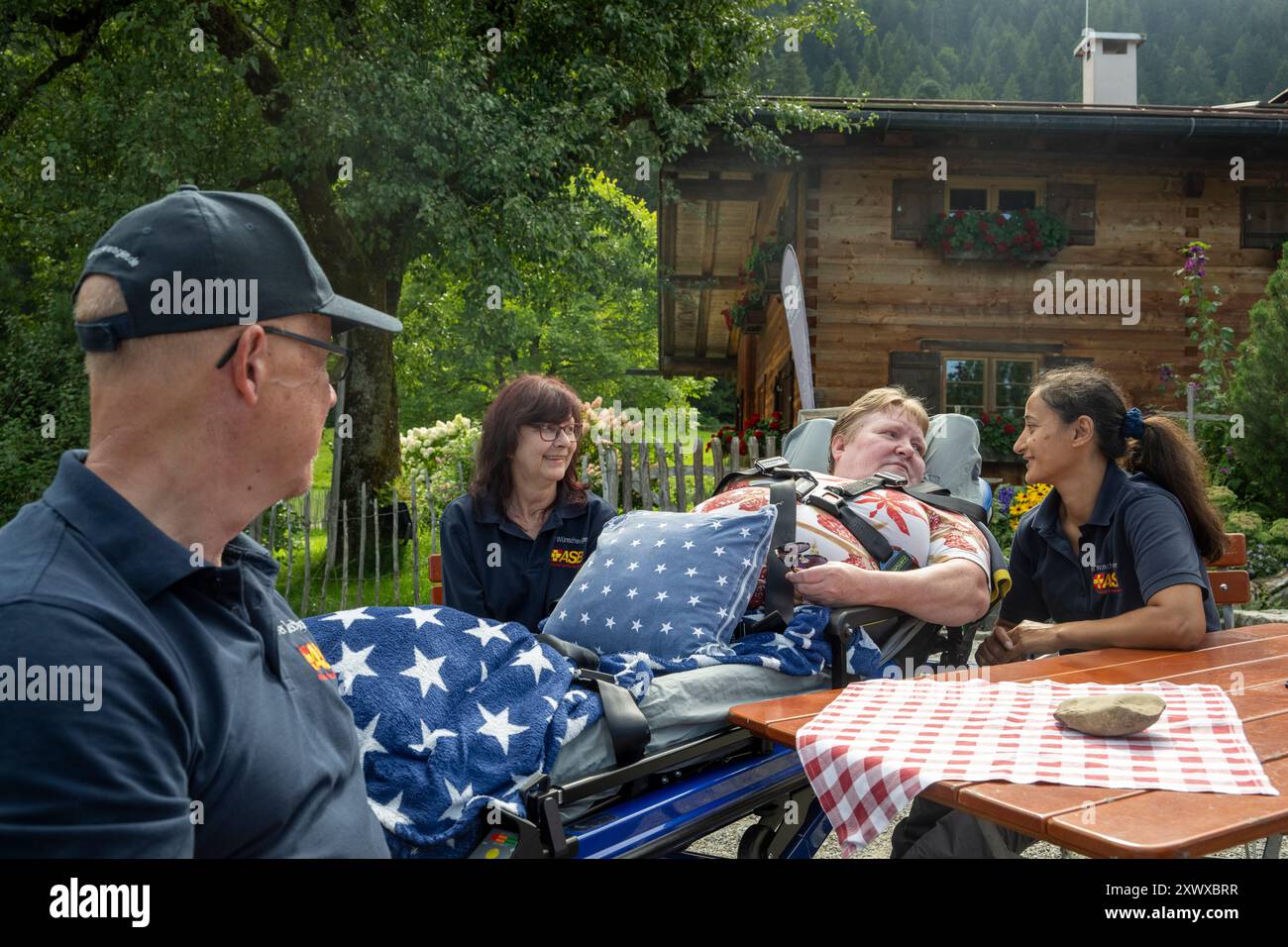 Oberstdorf, Deutschland. August 2024. Norbert Rzadki (l-r), Anita Sräga und Rima Schucht vom Arbeiter-Sarmariter-Bund (ASB) befinden sich auf der Alpe Dornach mit Kerstin Lindemann (2. Von rechts), die auf einer Liege liegt. Unter dem Motto „Dare to make Last wishes“ transportiert ASB Patienten, die sich einer Behandlung unterziehen, an besondere Orte, um ihre letzten Wünsche zu erfüllen und besondere Erlebnisse zu ermöglichen. Quelle: Stefan Puchner/dpa/Alamy Live News Stockfoto