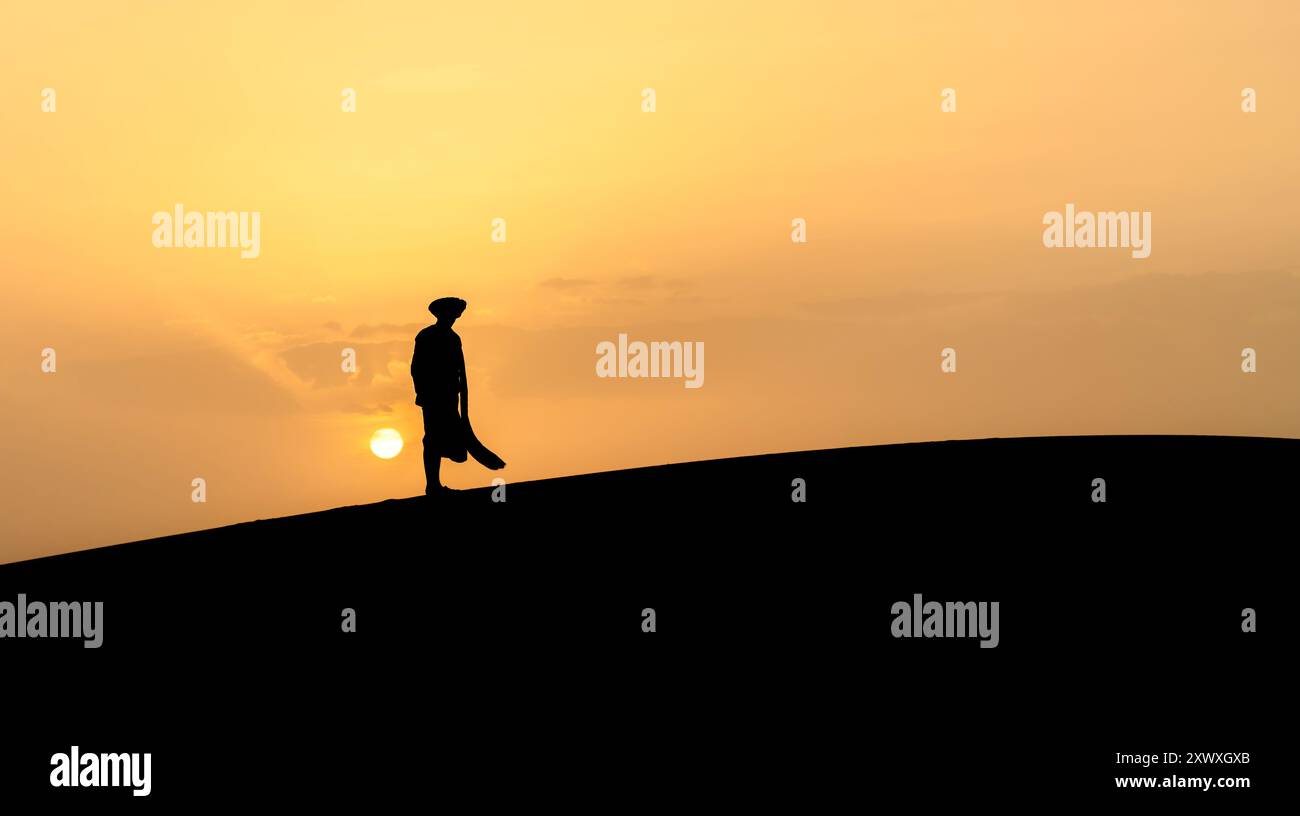 Silhouette eines nicht identifizierten Berbermanns in einem langen Gewand, der während eines atemberaubenden Sonnenuntergangs in der Sahara, Marokko, auf Sanddünen steht. Stockfoto