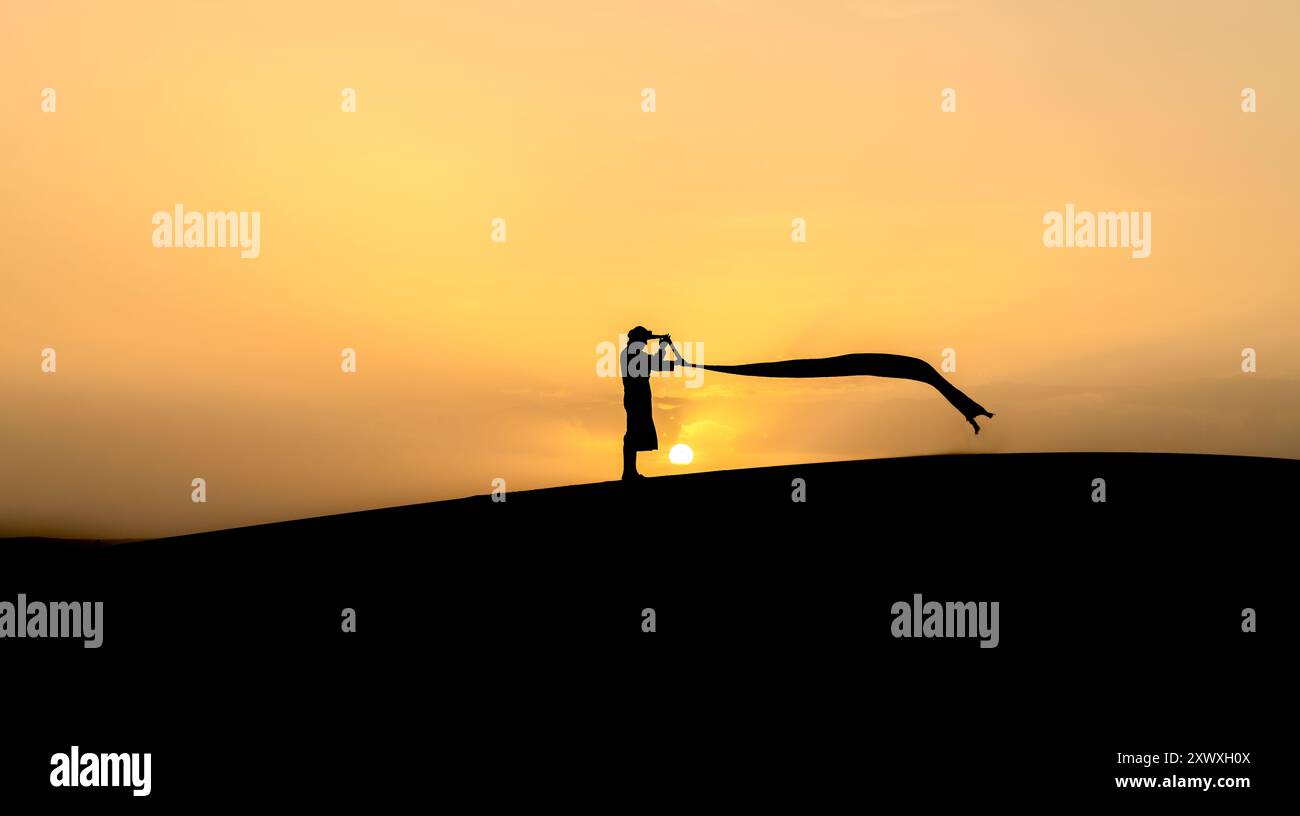 Silhouette eines nicht identifizierten Berbermannes in seinem langen Gewand und Turban, der im Wind auf Sanddünen bei schönem Sonnenuntergang in der Sahara, Marokko, schwingt Stockfoto