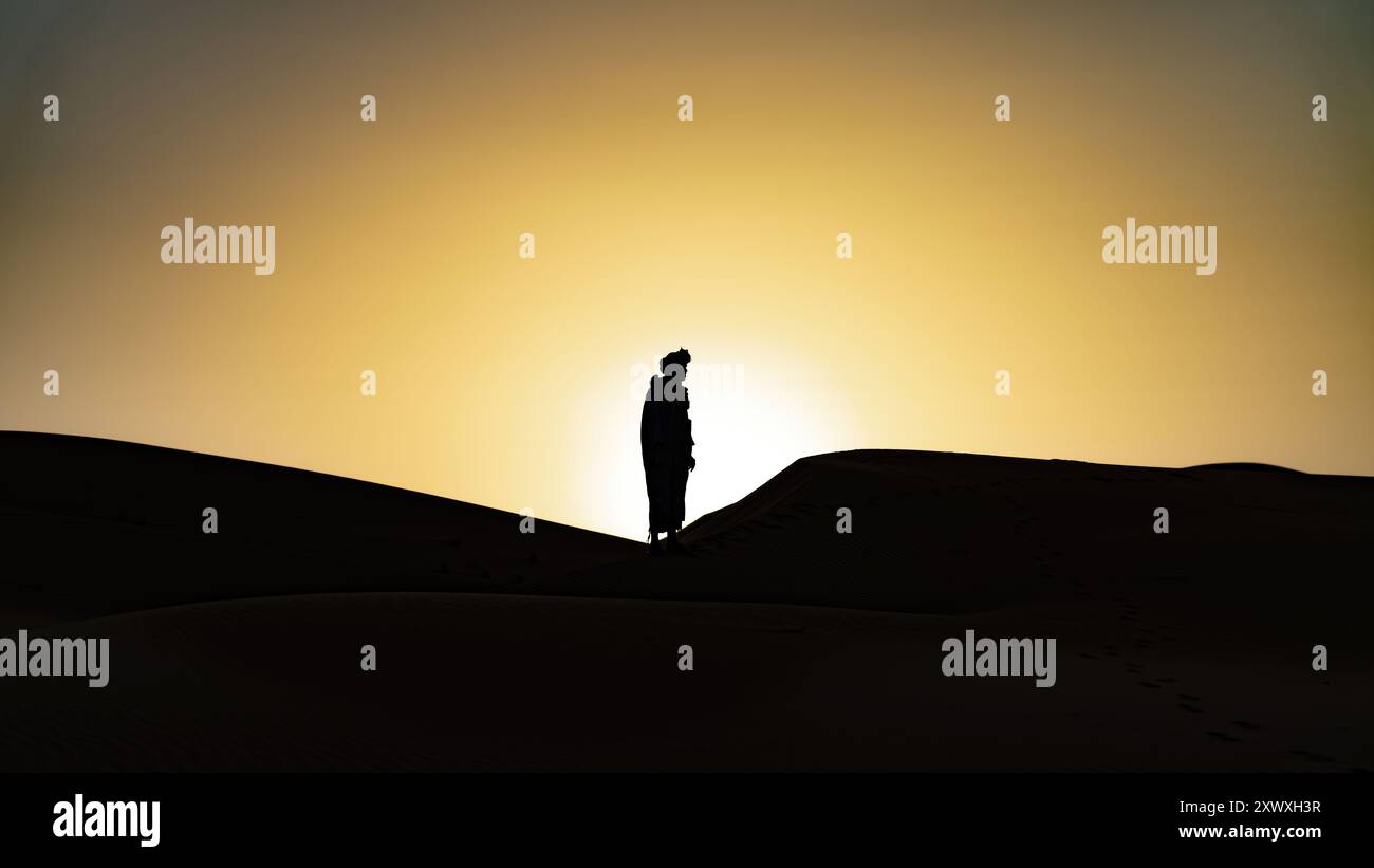 Silhouette eines nicht identifizierten Berbermanns in seinem traditionellen Gewand und Turban auf Sanddünen bei schönem Sonnenuntergang in der Sahara, Marokko Stockfoto