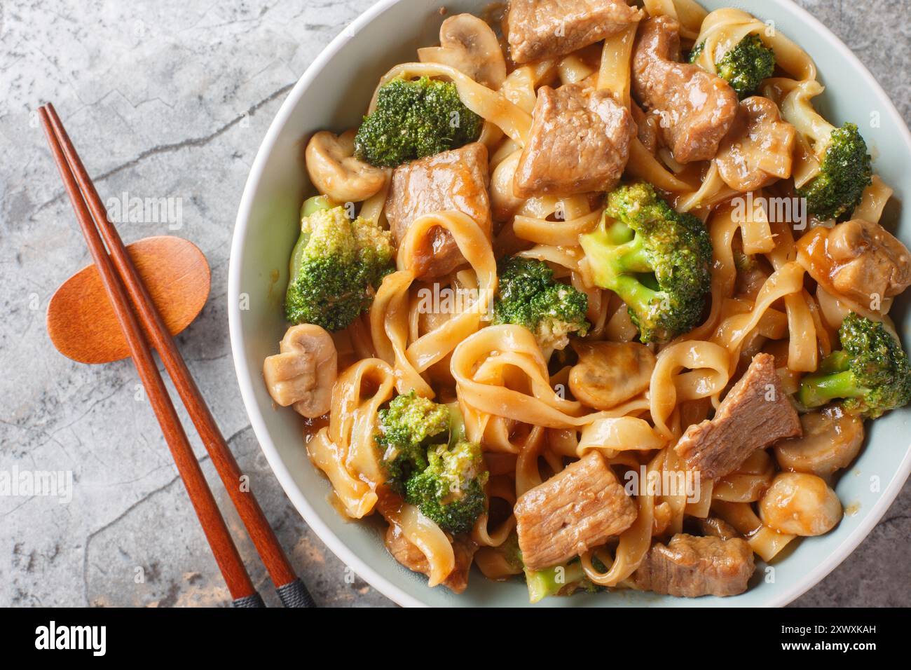 Asiatisches Pfannenbraten mit Rindfleisch, Brokkoli, Nudeln und Pilzen in Knoblauch-Sojasauce in der Nähe auf der Schüssel auf dem Tisch. Horizontale Draufsicht von oben Stockfoto