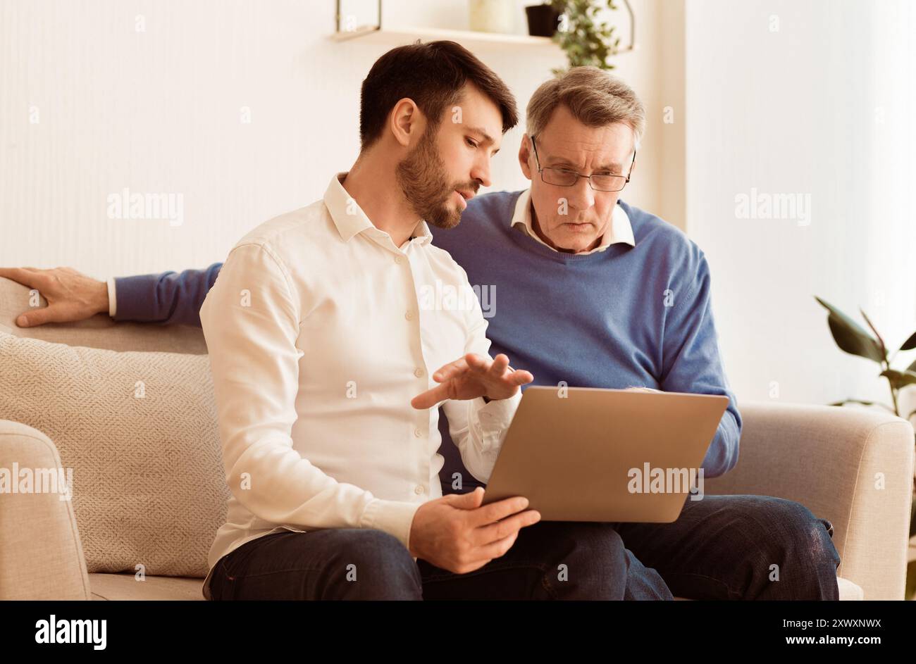 Middle-Aged Sohn Lehre Vater Setzen Laptop Indoor Stockfoto