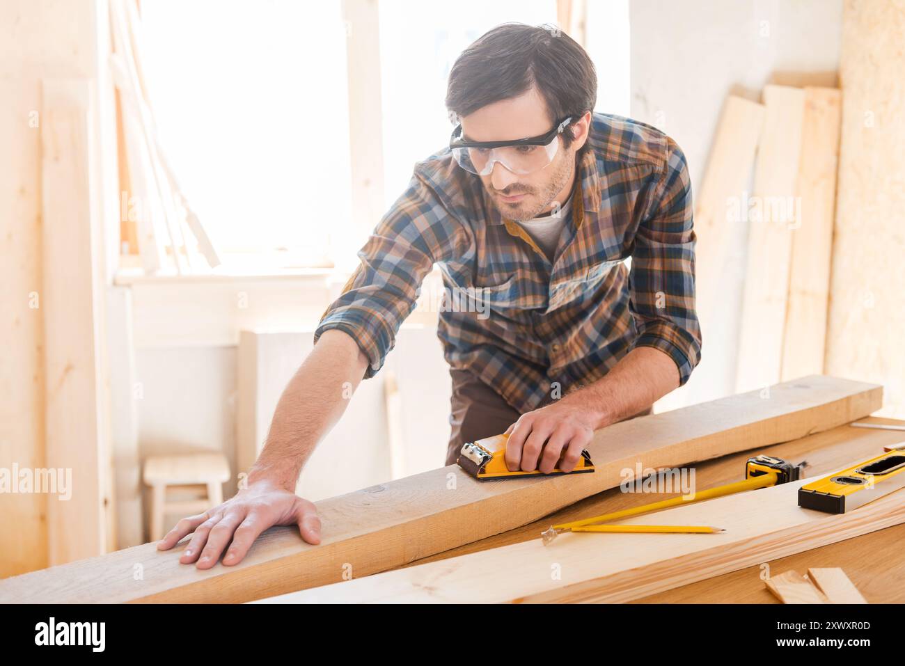 Alles sollte perfekt sein. Konzentrierter junger Zimmermann in Schutzbrille in seiner Werkstatt Stockfoto