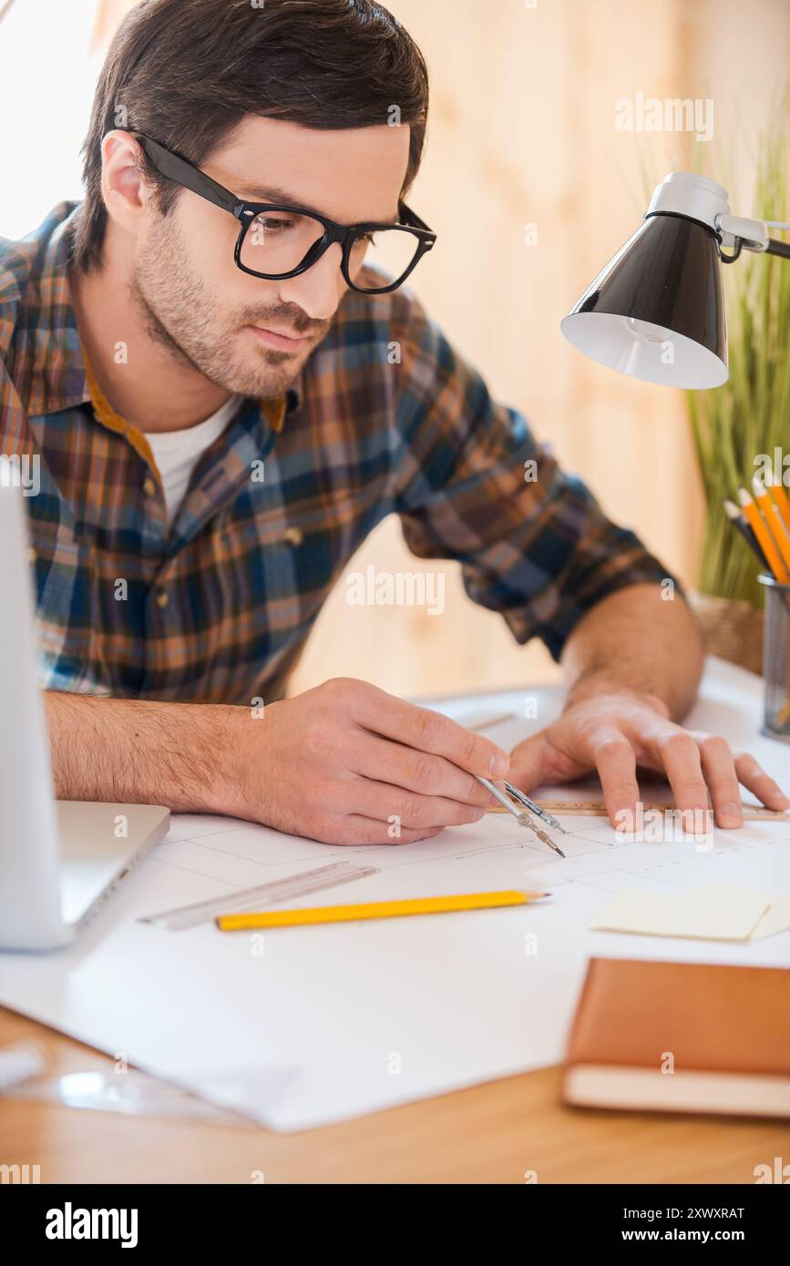 Seine Ideen in die Realität umzusetzen. Konzentrierter junger Mann, der Kompass zum Zeichnen benutzt, während er an seinem Arbeitsplatz sitzt Stockfoto