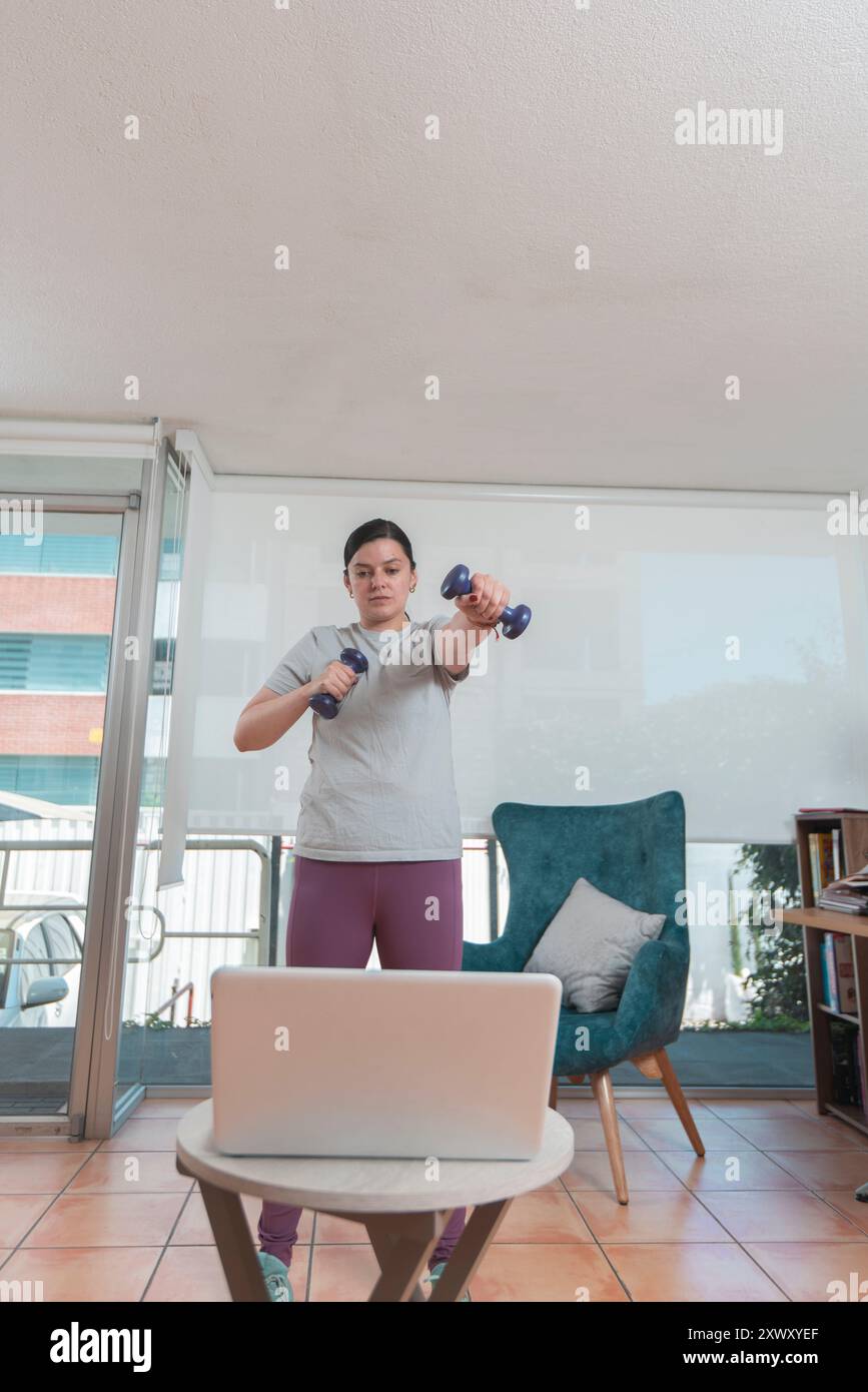 Schöne junge Latina Frau, die in ihrem Wohnzimmer vor ihrem Laptop nach einem Video-Tutorial während des Tages trainiert Stockfoto