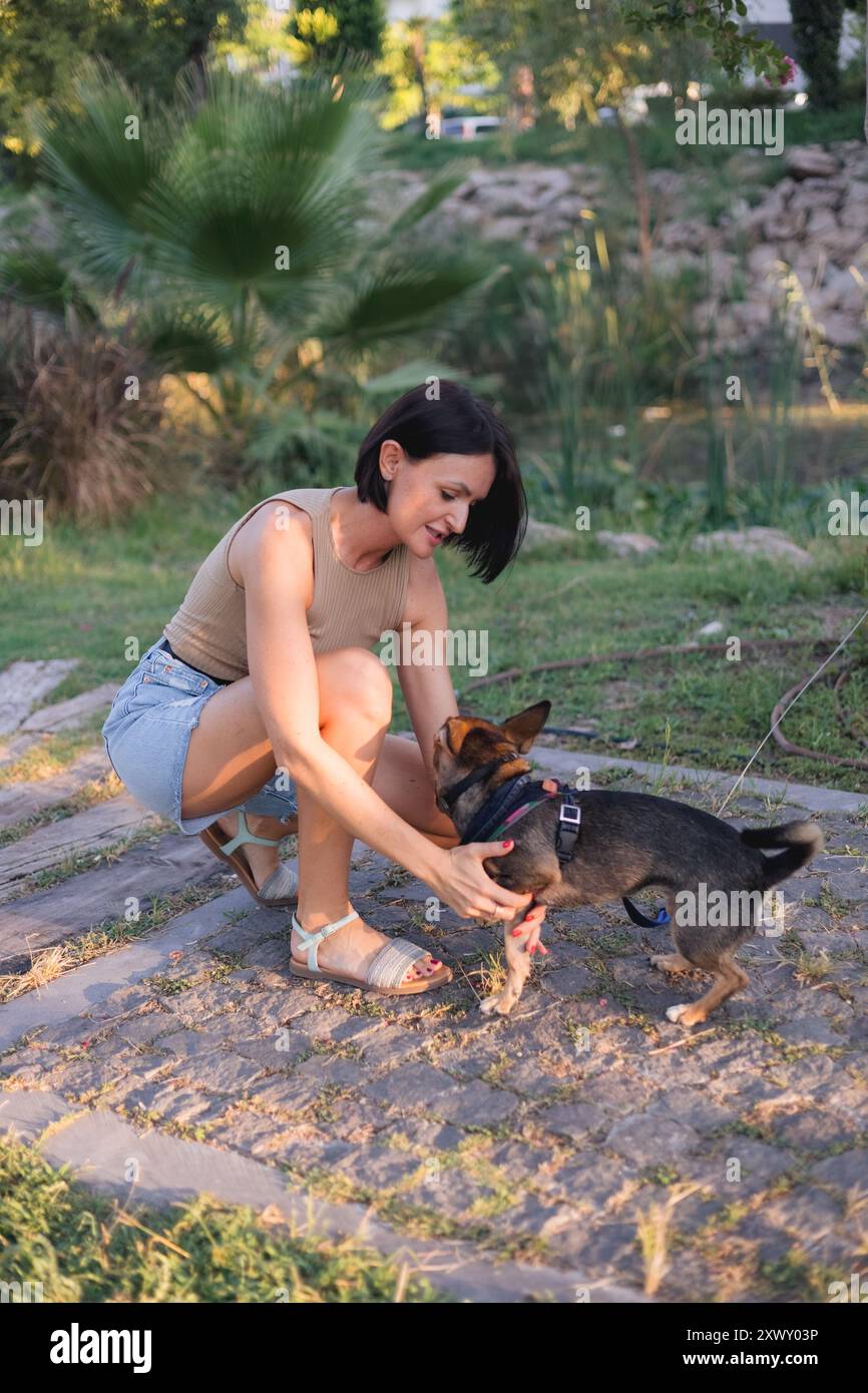 Lächelnde junge Frau geht und spielt mit einem kleinen Hund im öffentlichen Park. Stockfoto