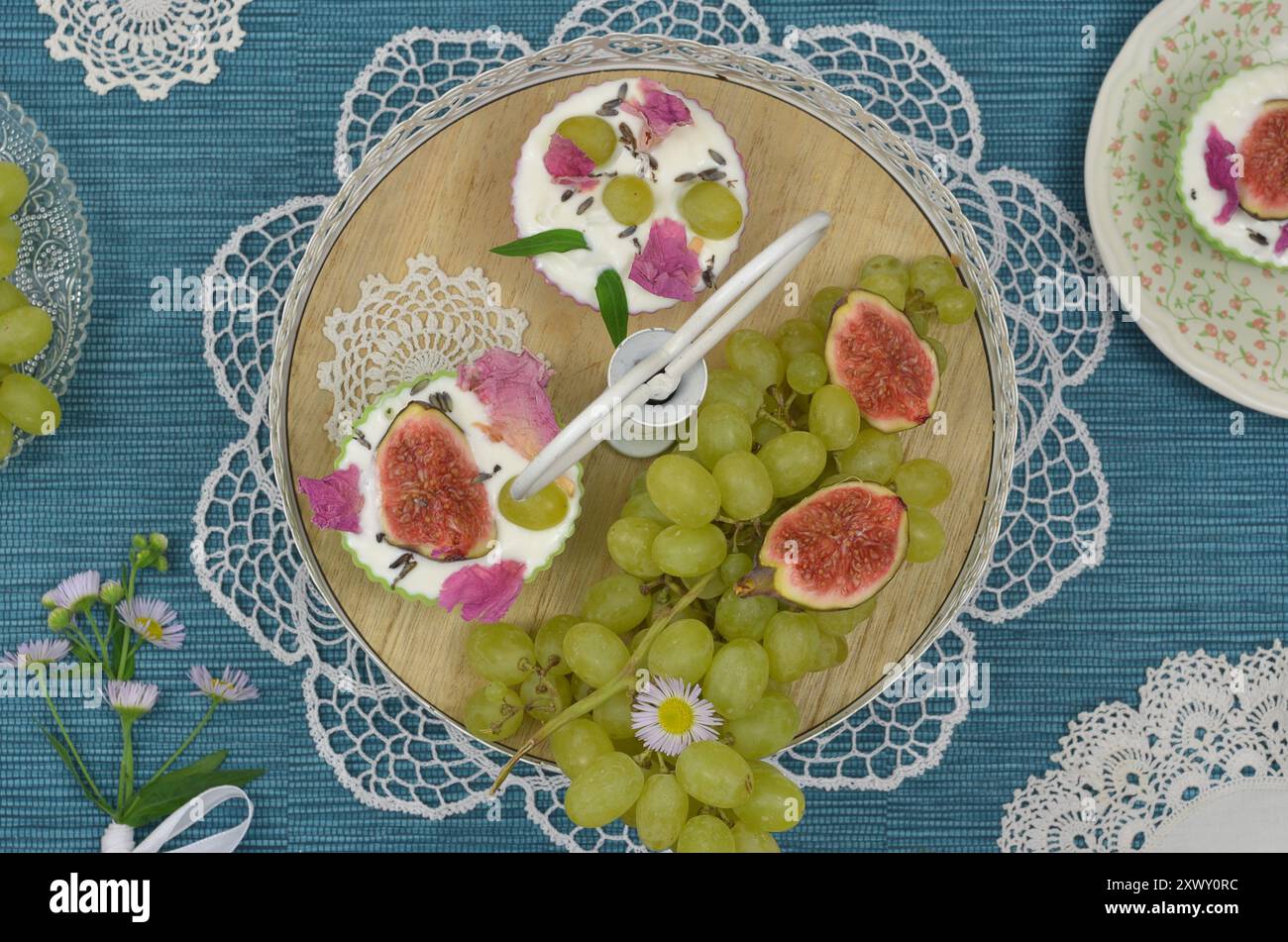 Cupcakes mit Sahne und Früchten auf einem Plateau, dekoriert mit Trauben, Feigen und Blumen. Blaue Tabelle, Draufsicht. Stockfoto