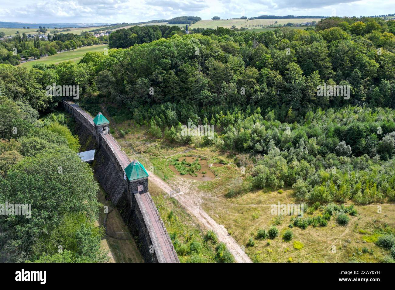 22. August 2024, Sachsen, Chemnitz: Blick auf die Staumauer des ehemaligen Euba-Stausees. Aufgrund baulicher Probleme kam das Klettern auf die Natursteinmauer vor rund 20 Jahren zum Stillstand. Gemeinsam mit der Sektion Chemnitz des Deutschen Alpenvereins konnten Mitglieder des Walden e.V. nun auf der gesicherten Außenseite einen neuen Klettergarten installieren. In den letzten Wochen wurden sieben gesicherte Routen in die bis zu 20 Meter hohe Staumauer gebohrt. Auch für die Zukunft ist ein Übungskletterweg geplant. Die Installation ist Teil eines Entwicklungsprozesses rund um den ehemaligen Damm. Im Fu Stockfoto