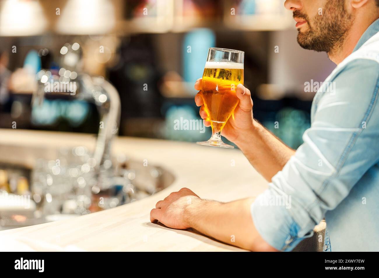 Genießen Sie das beste Bier der Stadt. Zugeschnittenes Bild eines jungen Mannes, der ein Glas Bier hält, während er an der Bar sitzt Stockfoto