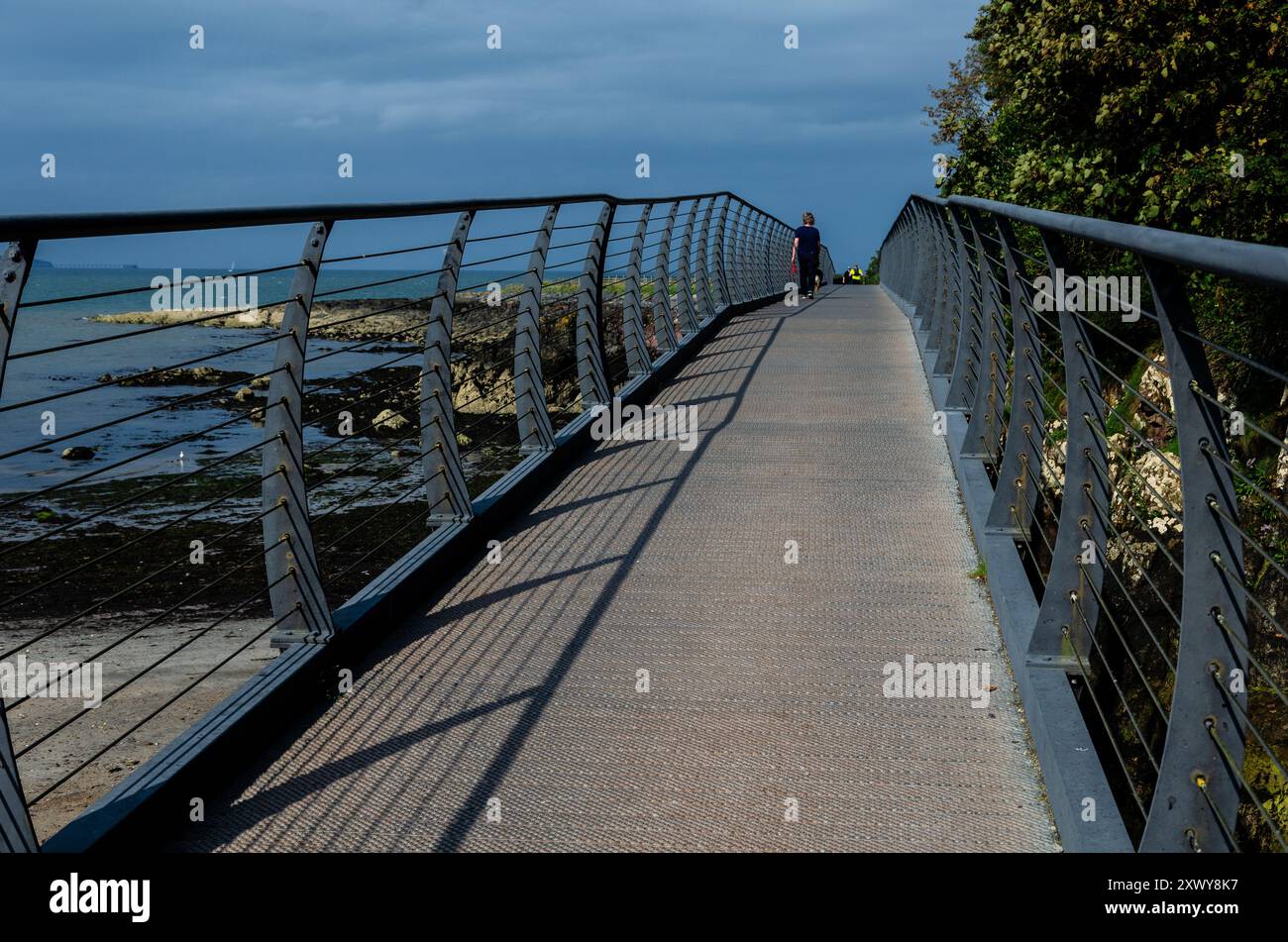 Fußgängerbrücke über die felsige Küste in County unten mit diagonalen Schatten, die von der Sonne geworfen werden Stockfoto