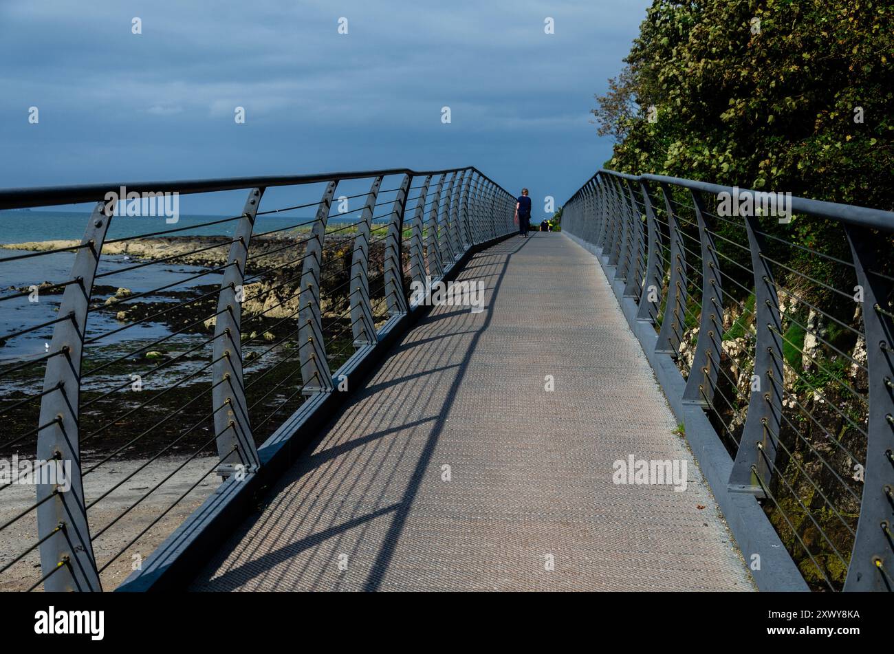 Fußgängerbrücke über die felsige Küste in County unten mit diagonalen Schatten, die von der Sonne geworfen werden Stockfoto