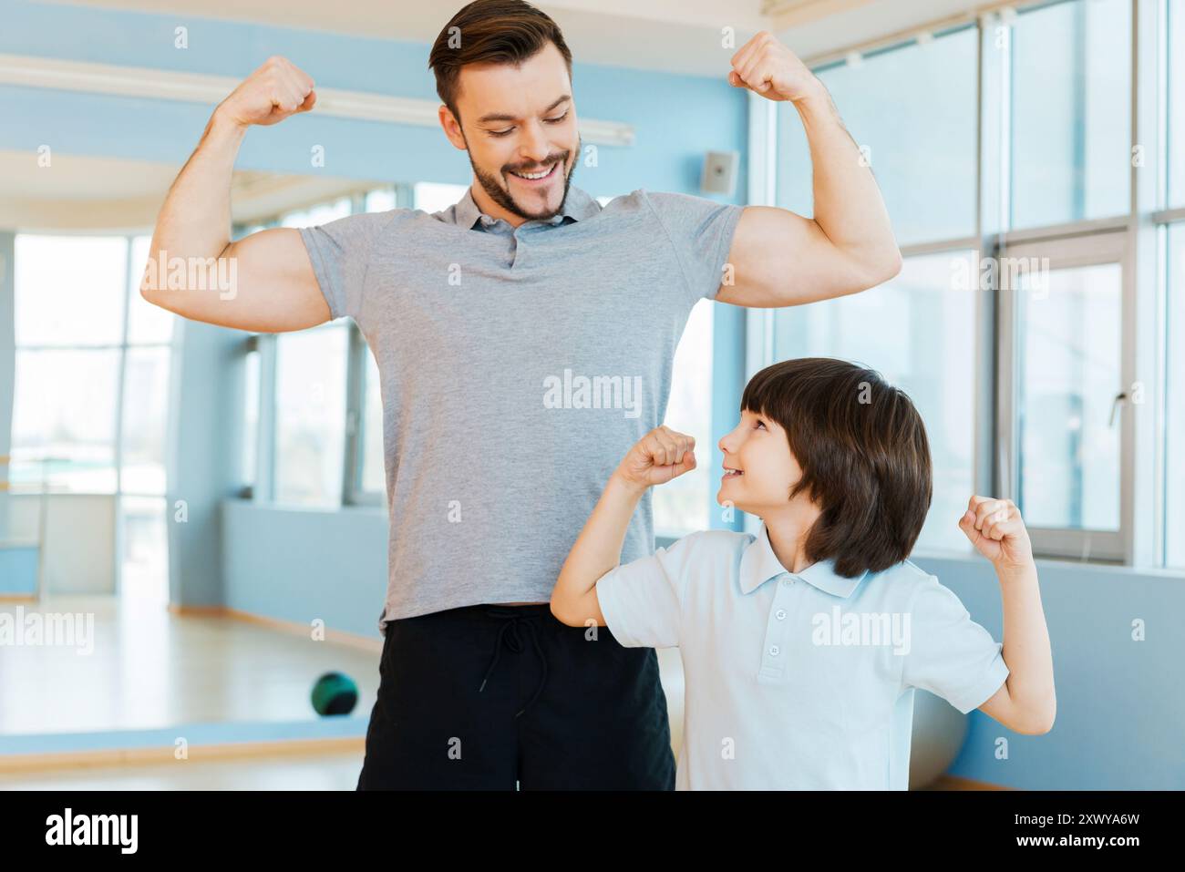 Stark und gesund. Glücklicher Vater und Sohn zeigen ihren Bizeps und lächeln, während sie beide im Health Club stehen Stockfoto