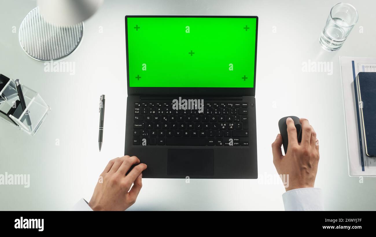 Anonymer Büromitarbeiter, der auf einem Laptop mit Mock-up-Green Screen Chromakey-Display mit Motion Tracker-Platzhaltern schreibt. Manager mit Geschäftspartnern per E-Mail. Top-Down-Ansicht Stockfoto