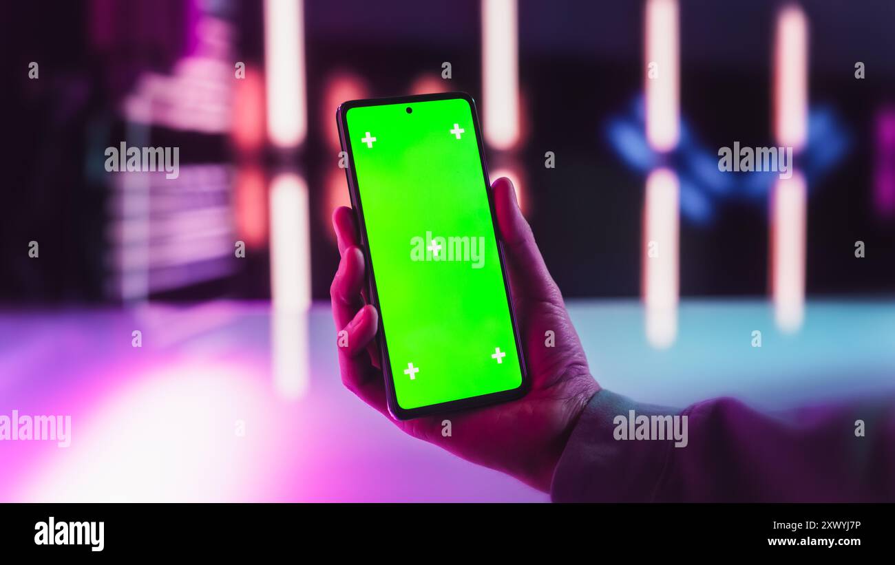 Anonymer Mann, der ein Smartphone mit einem Mock-Up Green Screen Chromakey Display in einem futuristischen Raum mit Neonlichtern hält. Fotovorlage mit Platzhalter für technische Werbe- und Unterhaltungsinhalte Stockfoto