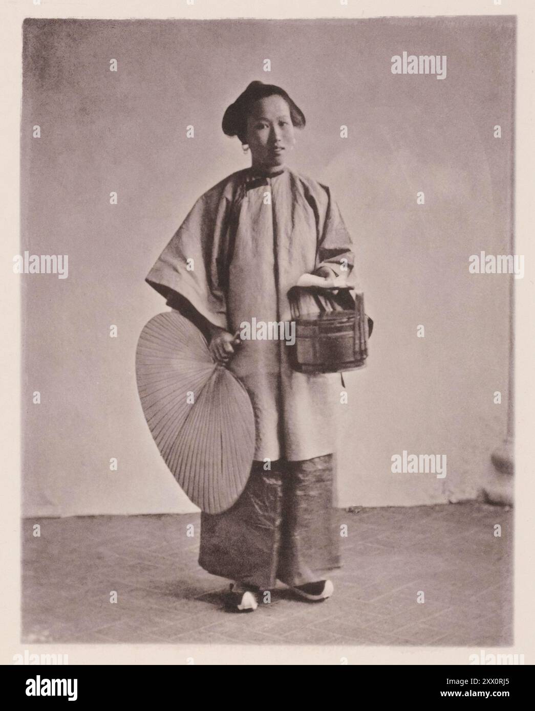 Vintage-Foto der chinesischen Dame in traditioneller Kleidung. Illustrations of Qing China, 1875 dieses Dienstmädchen ist ein Sklavenmädchen, das in der Kindheit für einen geringen Betrag von ihren armen Eltern gekauft wurde, da weibliche Kinder in vielen Teilen Chinas, wo noch immer Kindermord praktiziert wird, zu einem traurigen Rabatt kommen. Dieses Mädchen wurde im Busen der Familie aufgezogen und trainiert, auf die Damen des Haushalts zu warten, sich um die Kinder zu kümmern und sich allgemein nützlich zu machen. Auf diesem Bild ist sie auf dem Weg zum Markt dargestellt, die Sklavin genießt mehr Freiheit im Ausland als ihre Geliebte. In ihrer Linken Stockfoto