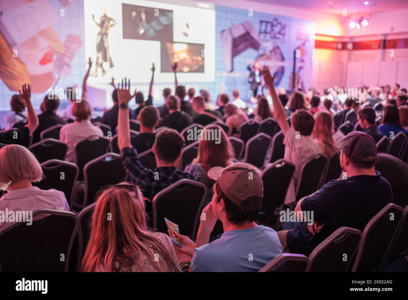 Begeistertes Publikum, das während der Konferenz der Präsentation zuhört. Die Menschen heben die Hände und sprechen mit dem Sprecher. Die Atmosphäre der Veranstaltung hebt die aktive Teilnahme und das Interesse hervor. Stockfoto