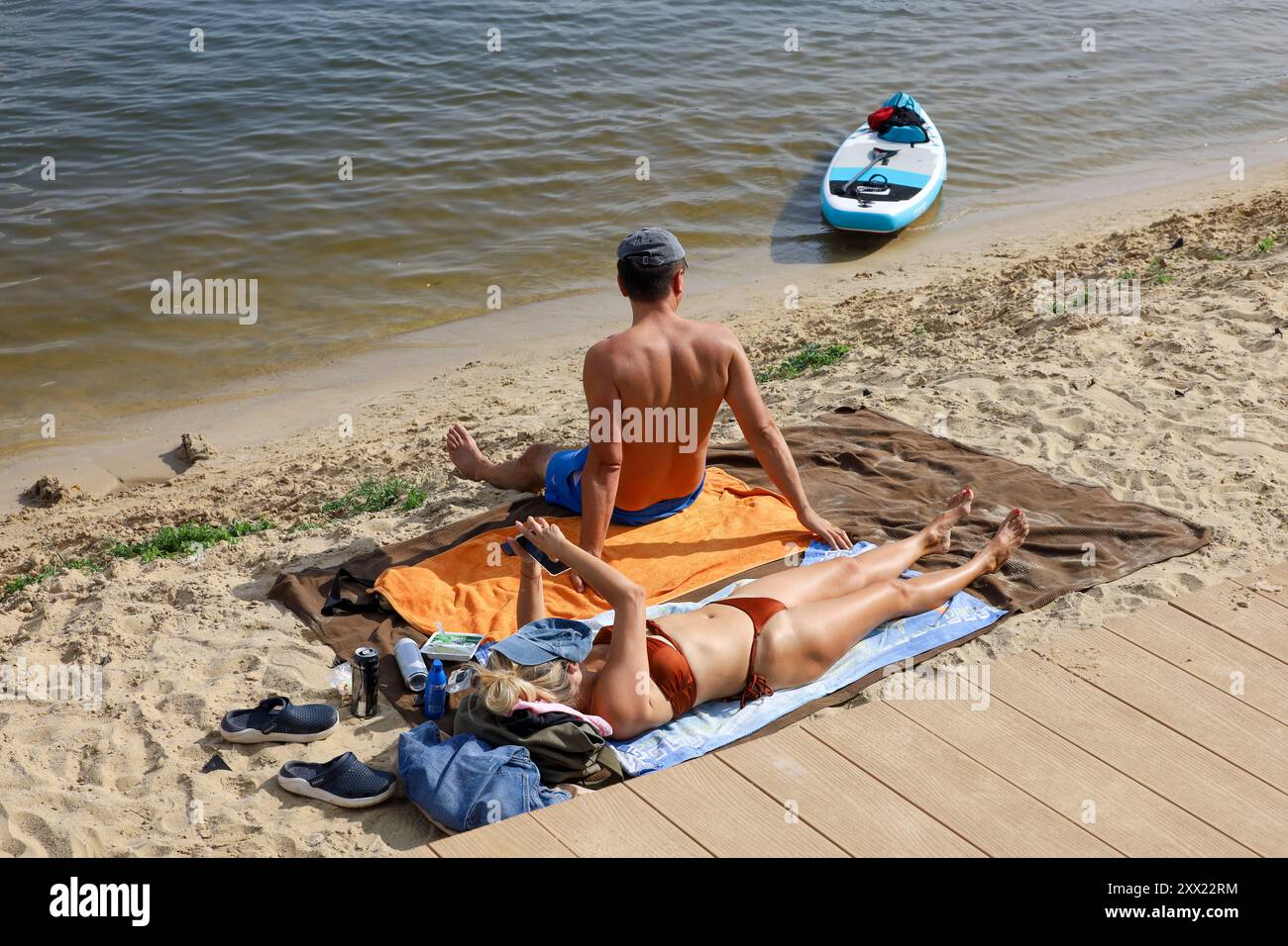Ein paar Sonnenbaden am Flussstrand. Heißes Wetter, Sommer-Picknick Stockfoto