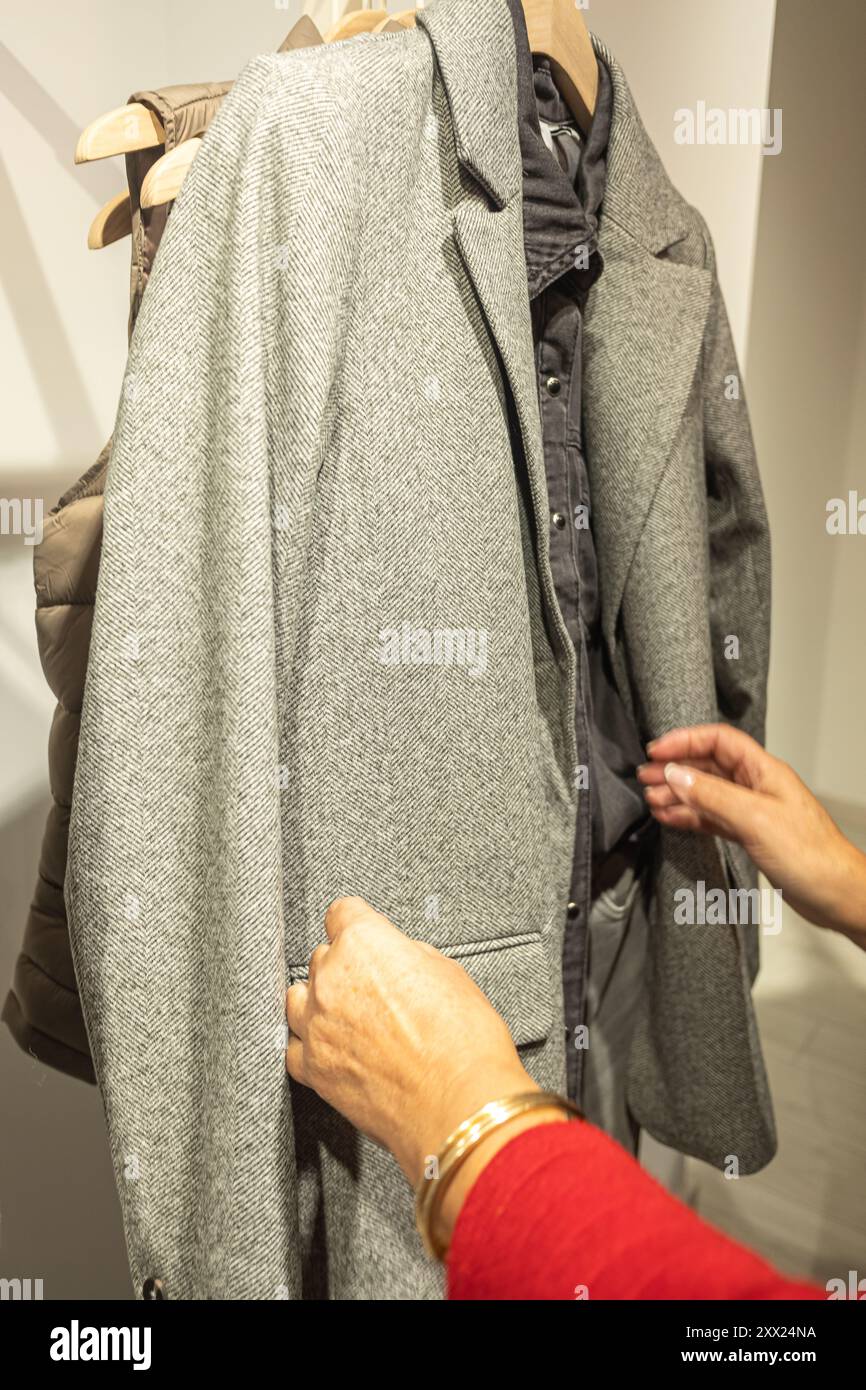 Frauenhände schauen sich eine herbstliche Jacke an, die an einem Kleiderbügel in einem Bekleidungsgeschäft hängt Stockfoto