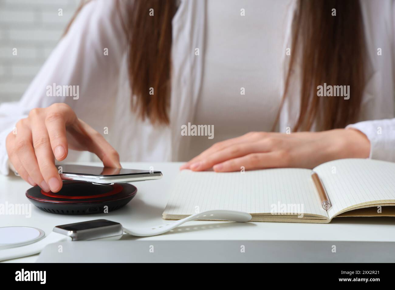 Frau, die modernes Handy auf das kabellose Ladegerät auf dem Tisch legt, Nahaufnahme Stockfoto
