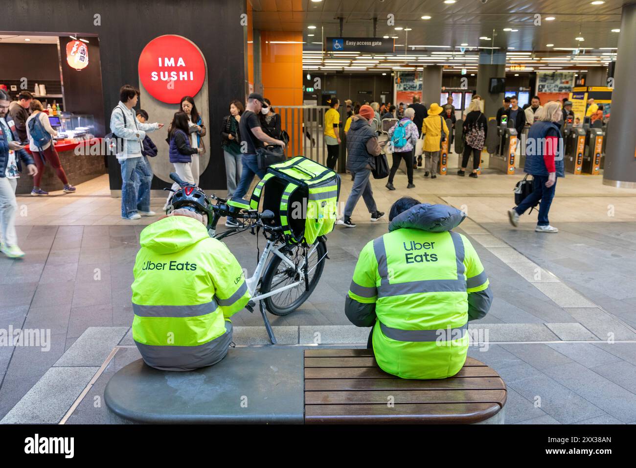 Die Fahrer von Uber Eats machen eine Mittagspause in Chatswood Sydney mit Elektro-E-Bike neben ihnen, in hiviz gelben Jacken, Chatswood, Sydney Stockfoto