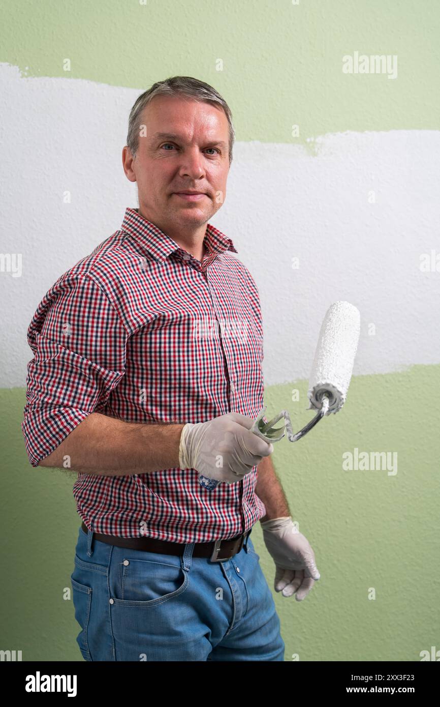 Ein Mann malt grüne Wände mit weißer Farbe mit einer Walze. Bauarbeiten und Kosmetikreparaturen im Haus, Wandmalerei, Abschlussarbeiten mit Ihrem Rew Stockfoto