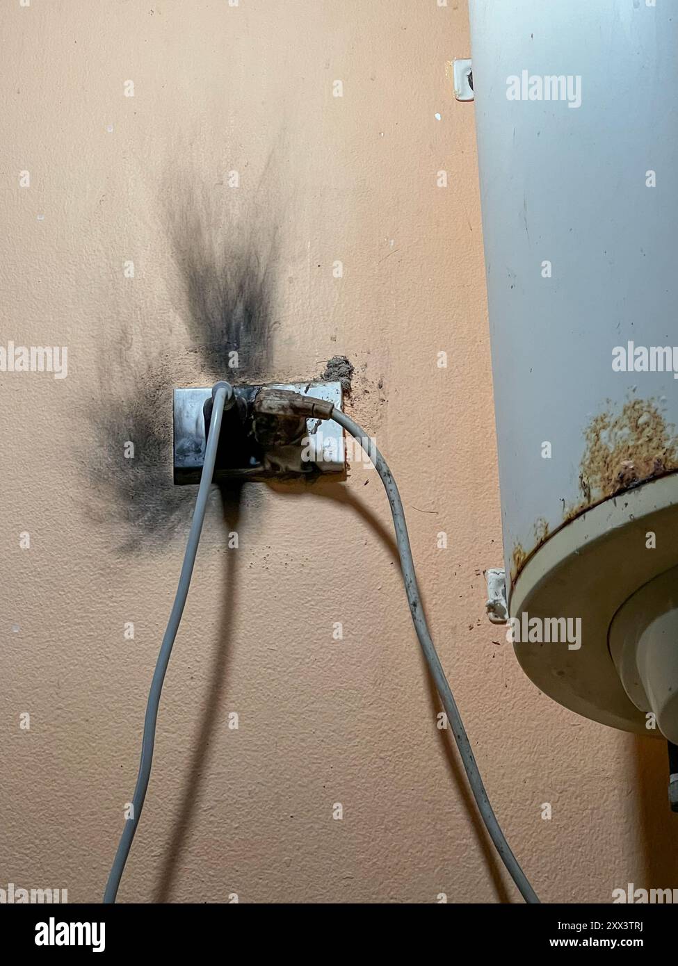 Dieses Foto zeigt eine verbrannte Steckdose mit schwarzem Ruß an der Wand, was auf einen Kurzschluss oder einen elektrischen Brand hinweist. Zwei Kabel sind noch angeschlossen Stockfoto