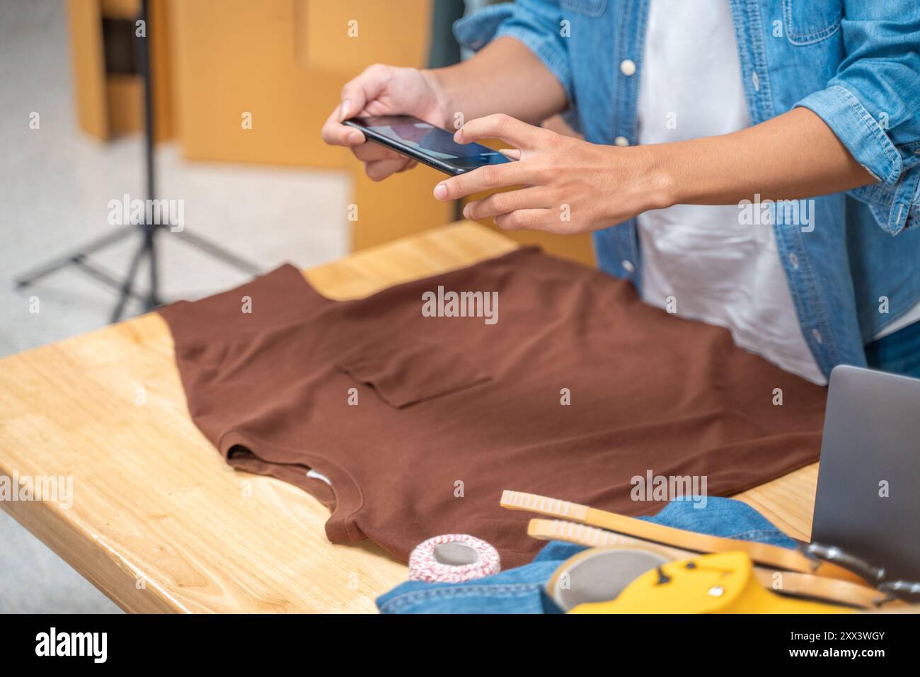 Junger Online-Verkäufer, der mit seinem Handy Fotos von seinem Hemdprodukt macht und ihn von seinem Heimstudio an seine Kunden sendet Stockfoto