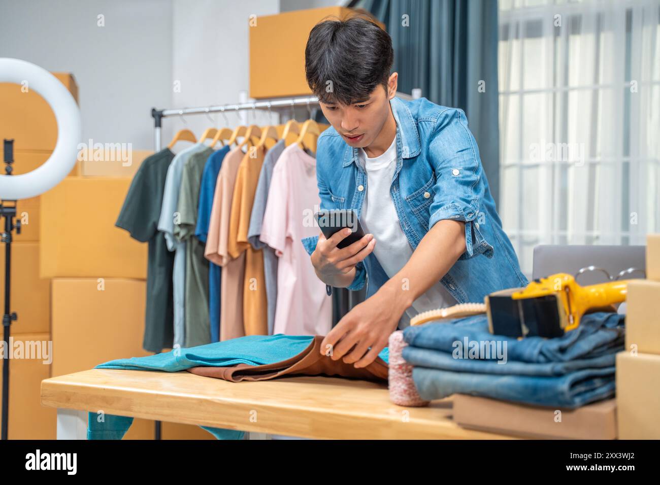 Junger Online-Verkäufer, der mit seinem Handy Fotos von seinem Hemdprodukt macht und ihn von seinem Heimstudio an seine Kunden sendet Stockfoto