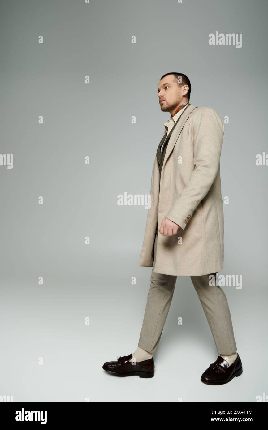 Ein stilvoller Mann in einem beigefarbenen Trenchcoat geht selbstbewusst über eine minimalistische Kulisse. Stockfoto