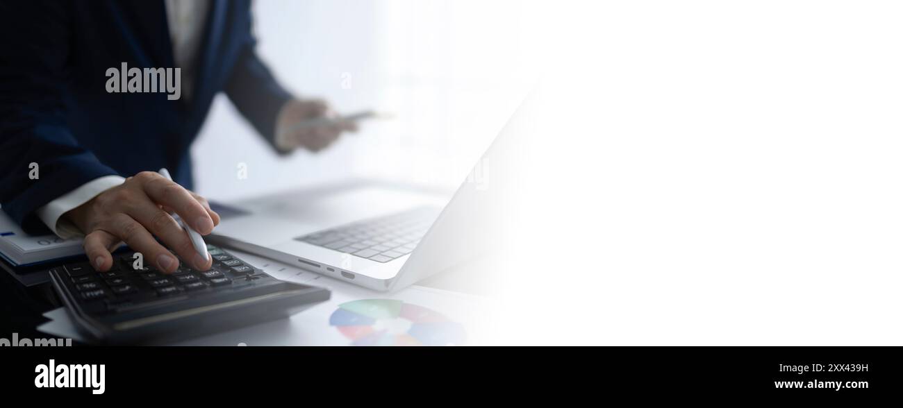 Ein Geschäftsmann beschäftigt sich mit Finanzanalysen und Geschäftsplanung mithilfe eines Rechners und Laptops. Das Bild zeigt ein professionelles Umfeld Stockfoto