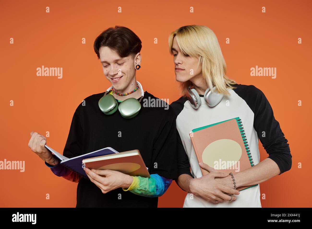 Zwei junge queere Freunde in bunten Outfits studieren zusammen vor einem orangen Hintergrund. Stockfoto