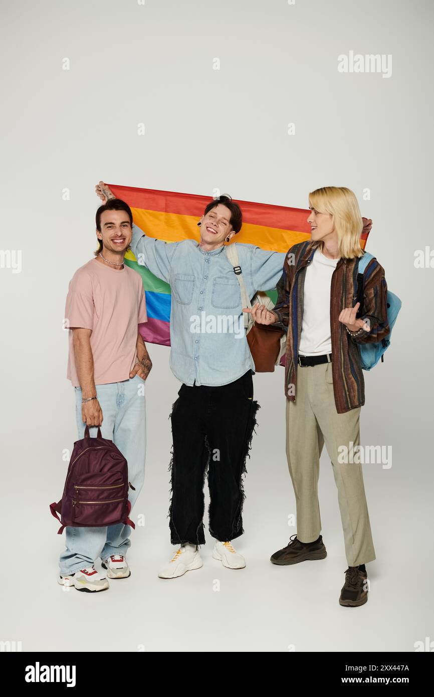 Drei junge Studenten, die Teil der LGBTQIA-Community sind, stehen zusammen und halten eine Regenbogenfahne. Stockfoto