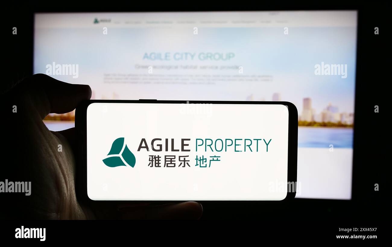 Person, die ein Mobiltelefon mit dem Logo des chinesischen Unternehmens Agile Property Holdings Limited vor der Webseite hält. Schwerpunkt auf dem Display des Telefons. Stockfoto