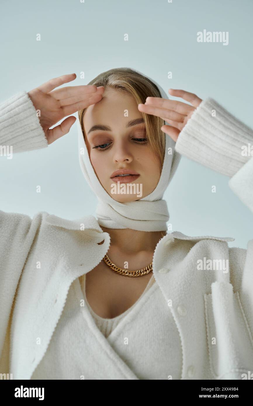 Eine Frau in weißem Strickoutfit und Schal posiert mit kontemplativem Ausdruck. Stockfoto