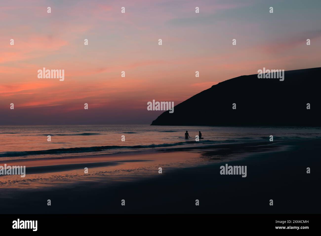 Wunderschöner Sonnenuntergang über Cornwall Beach mit Silhouette von Surfern, ruhiger Abendhimmel, der sich auf ruhigem Wasser spiegelt, malerische britische Küste, perfekt für trave Stockfoto