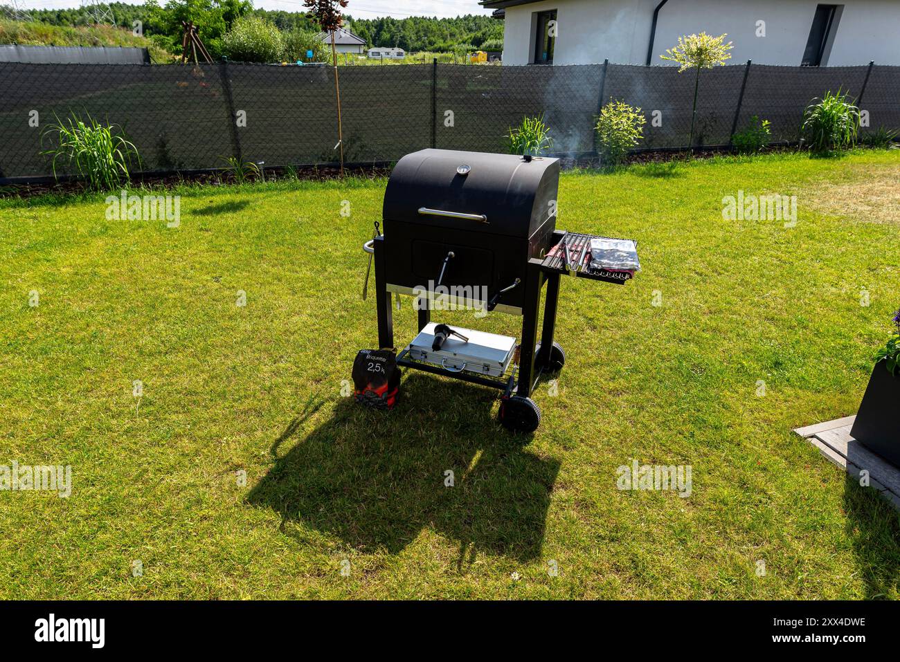 Rauch steigt von einem modernen geschlossenen Grill auf einem wunderschönen grünen Rasen. Stockfoto